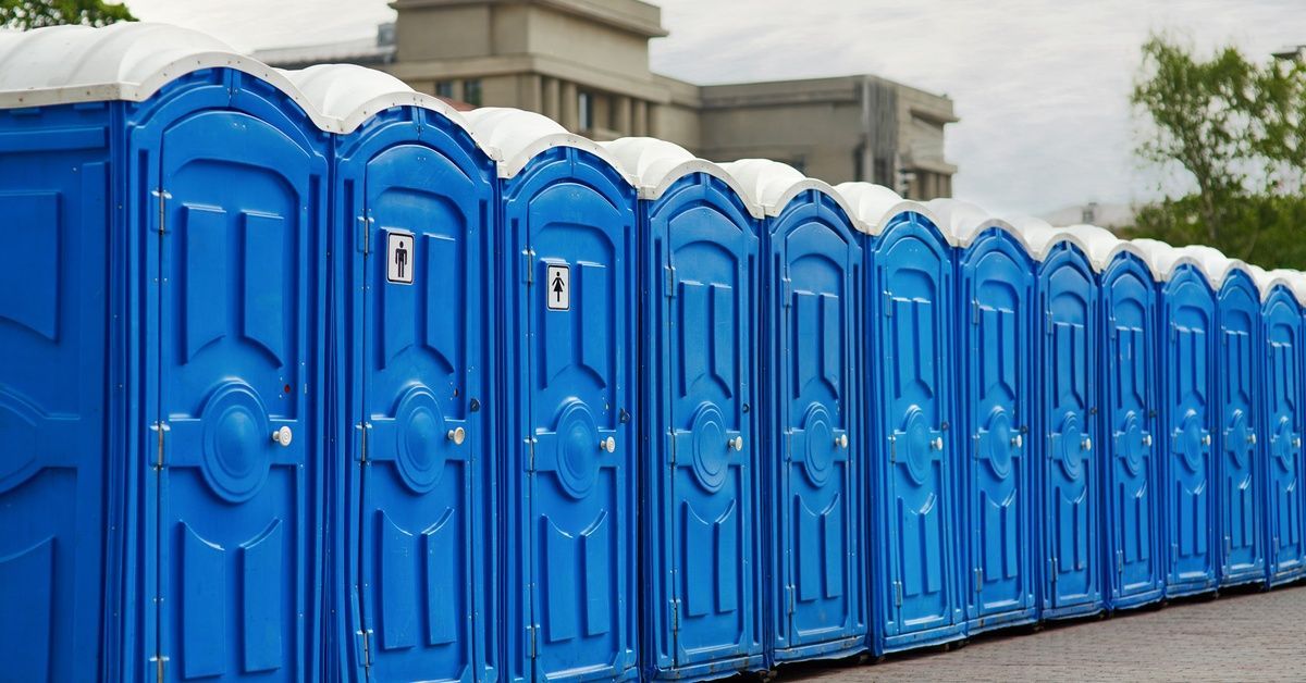 A row of blue portable toilets outside at an event. One unit has a male figure, and another has a female figure on the door.