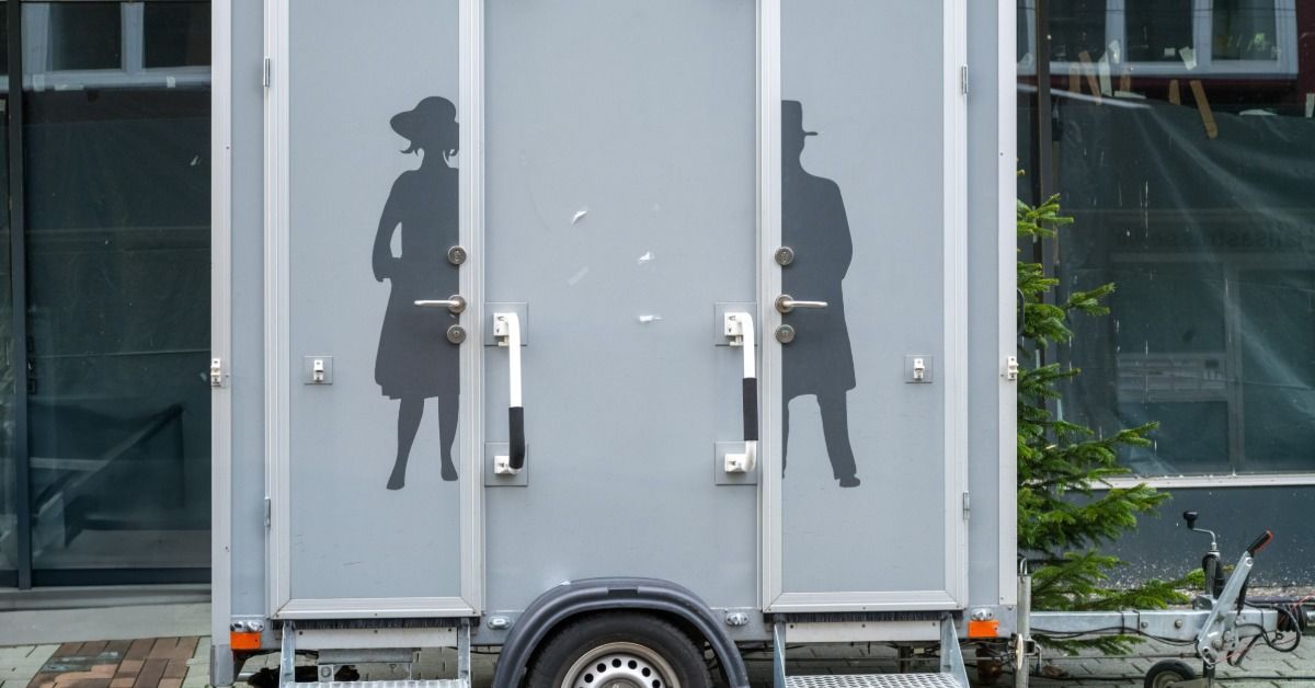A two-person restroom trailer sits outside at a wedding. The restroom doors feature male and female decals.