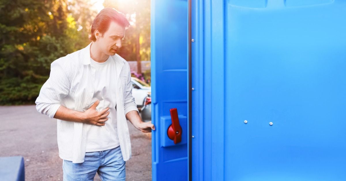 A male festival attendee makes his way into the portable restroom. The restroom unit is blue with a red handle.