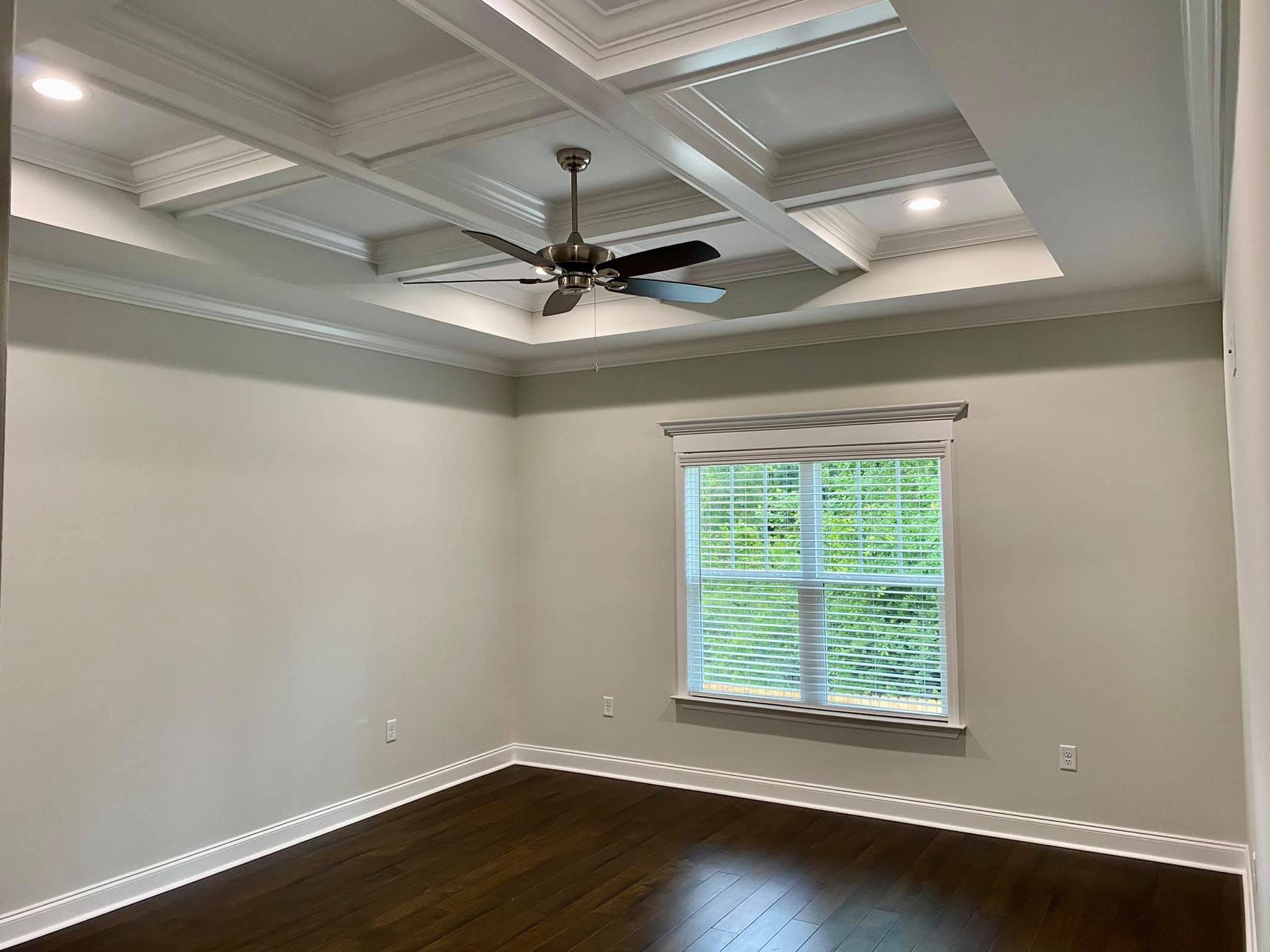 Empty room with dark wood floor, light gray walls, and ornate ceiling. Window with blinds is in the middle.