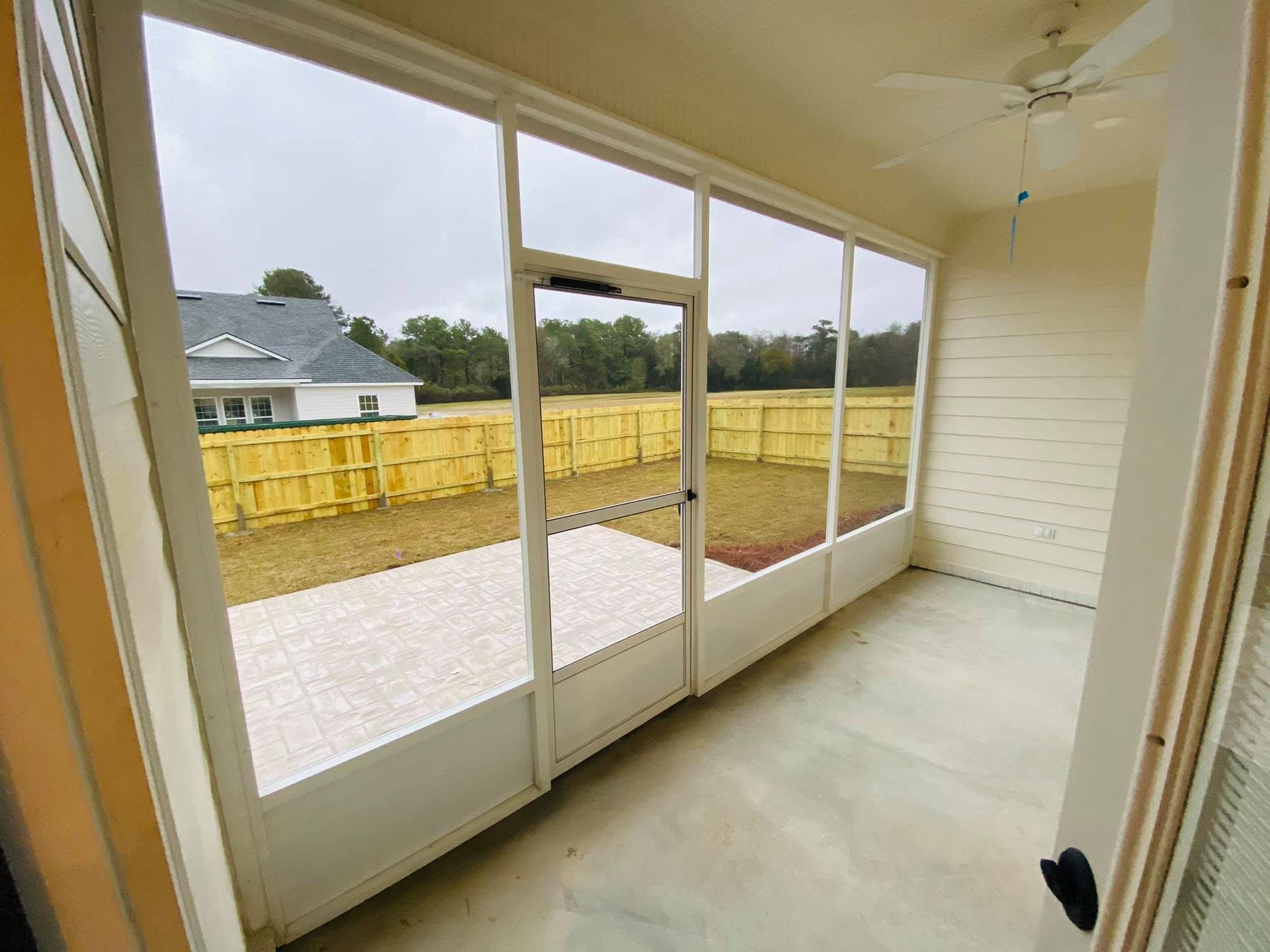 Sunroom with screen walls, door, and patio flooring, overlooking a backyard with a yellow fence.