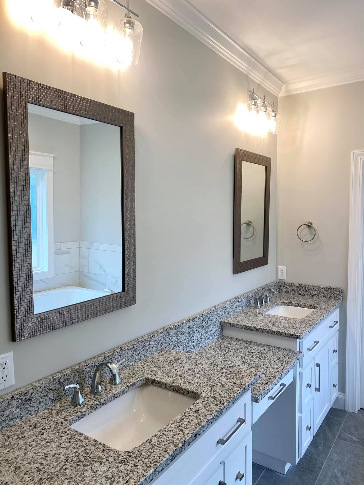 Bathroom with two vanities, granite countertops, mirrors, and bright lighting.
