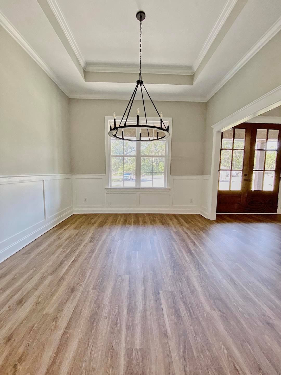 Empty dining room with wood floors, chandelier, and white wainscoting. Beige walls and a dark wood door.