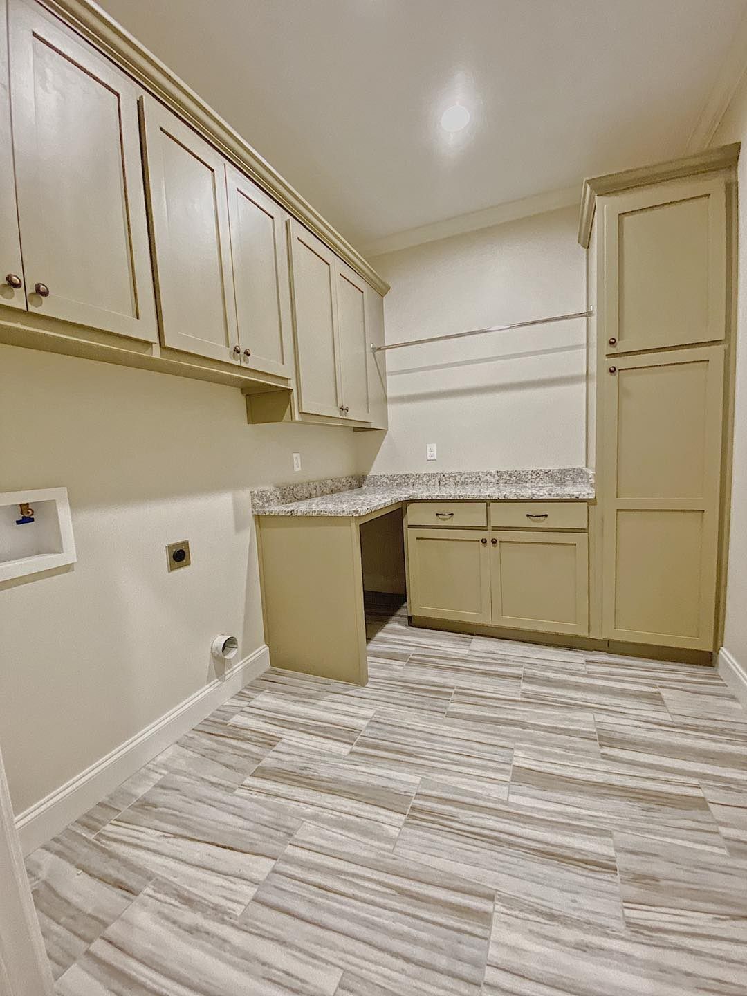Laundry room with light green cabinets, granite countertop, and wood-look tile flooring.