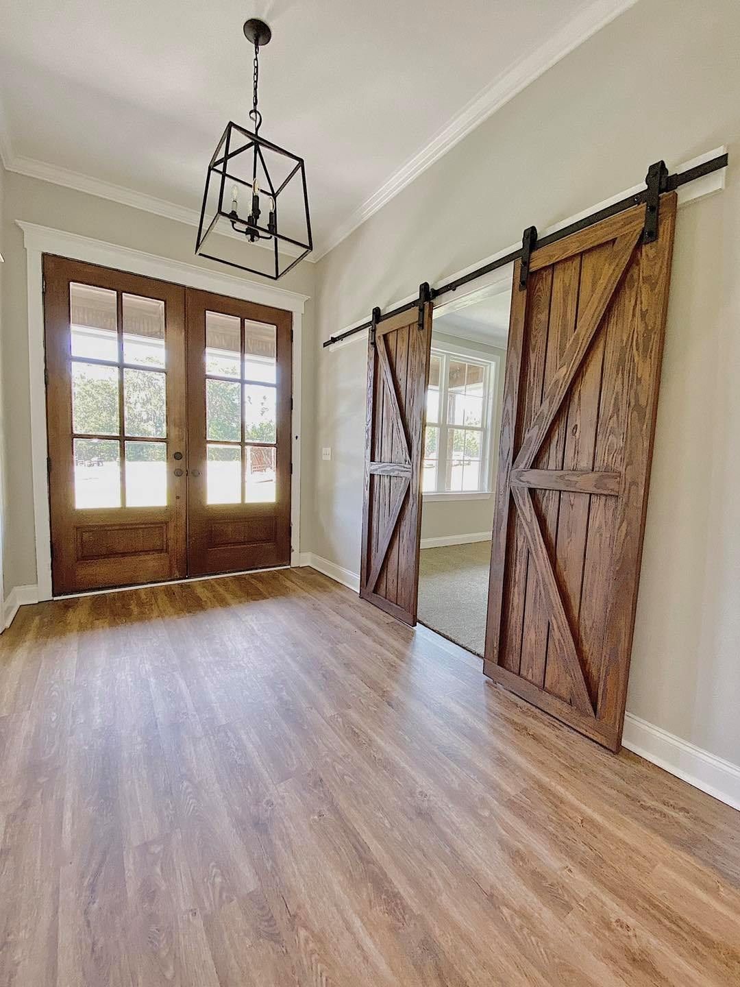 Wooden barn doors, French doors, chandelier, wood floor, and gray walls.