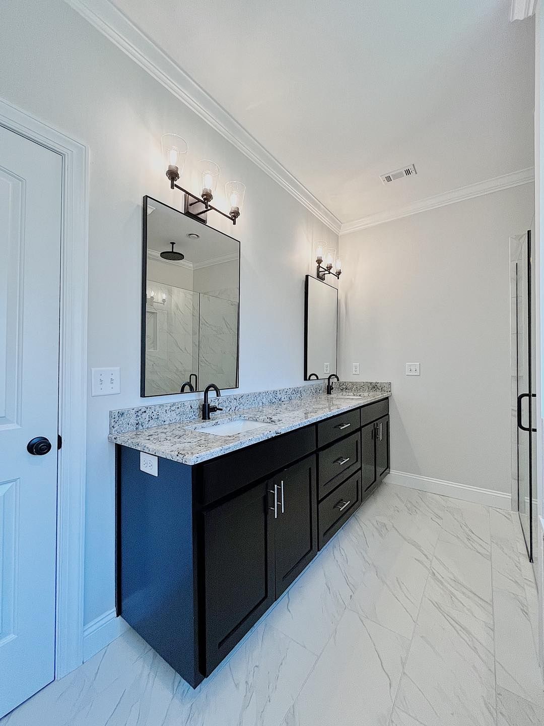 Bathroom with black double vanity, granite countertop, two mirrors, and marble tile floor.