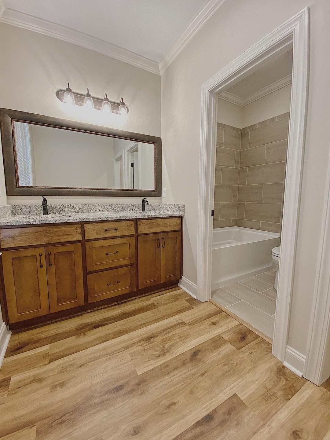 Bathroom with a wooden vanity, a large mirror, and an open doorway to a tub and shower.