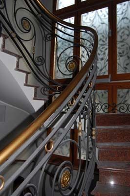 Elegante scala interna con ringhiera in ferro battuto nero decorata e gradini in legno accanto a una porta in vetro satinato.