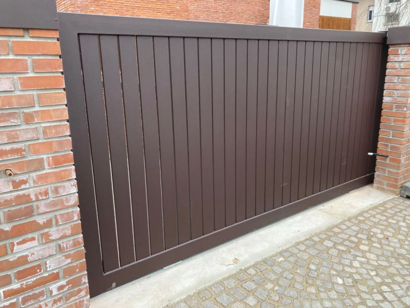Cancello di legno marrone tra muri di mattoni accanto a un sentiero lastricato.