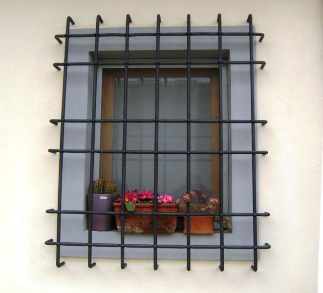 Finestra con inferriate in metallo nero e vasi di fiori sul davanzale, addossata a una parete chiara.