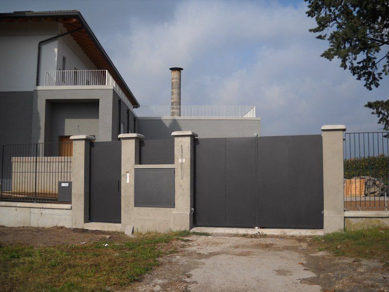 Casa moderna dietro un cancello e una recinzione grigi sotto un cielo parzialmente nuvoloso