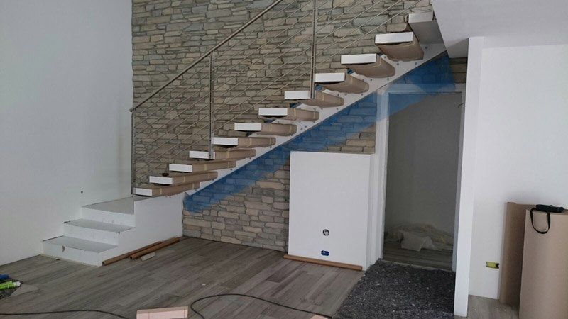 Scala interna con gradini bianchi e muro in mattoni, zona in costruzione con isolamento blu a vista e armadio sotto le scale