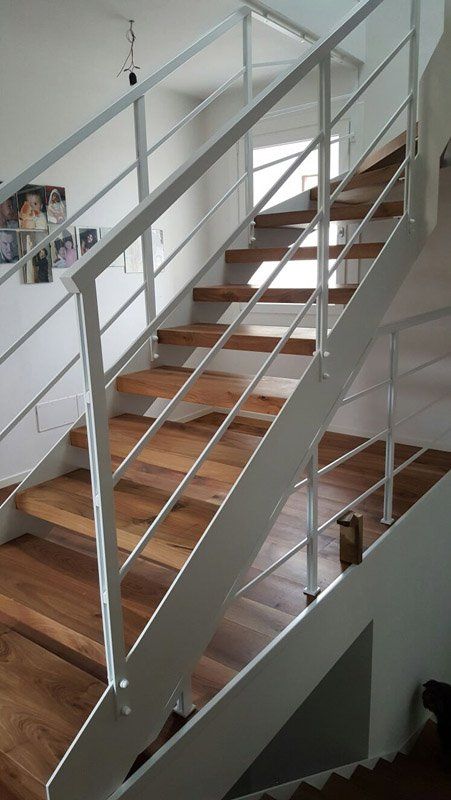 Scala interna con gradini in legno, ringhiere bianche e travi di supporto in metallo in una casa moderna