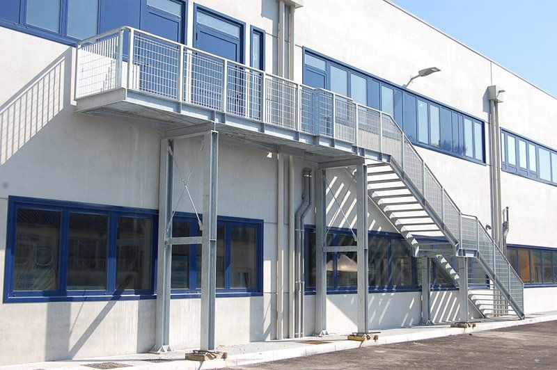 Esterno moderno dell'edificio con finestre blu, scala in metallo e passerella con balcone.