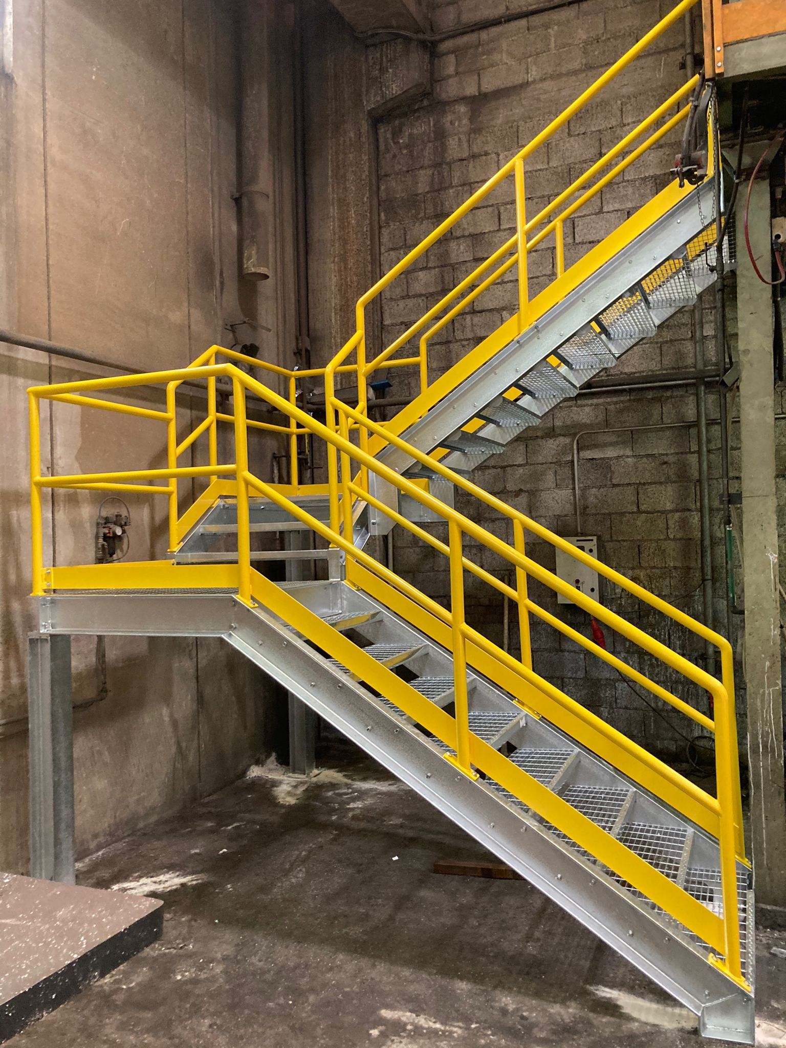 Scala metallica gialla con ringhiera in un interno industriale in cemento.