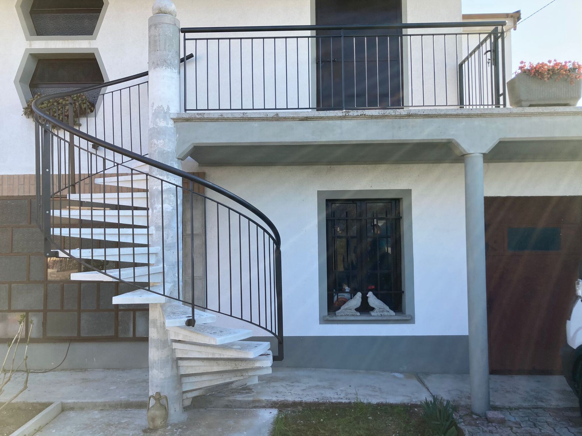 Esterno di una casa con scala curva, balcone e porta del garage.