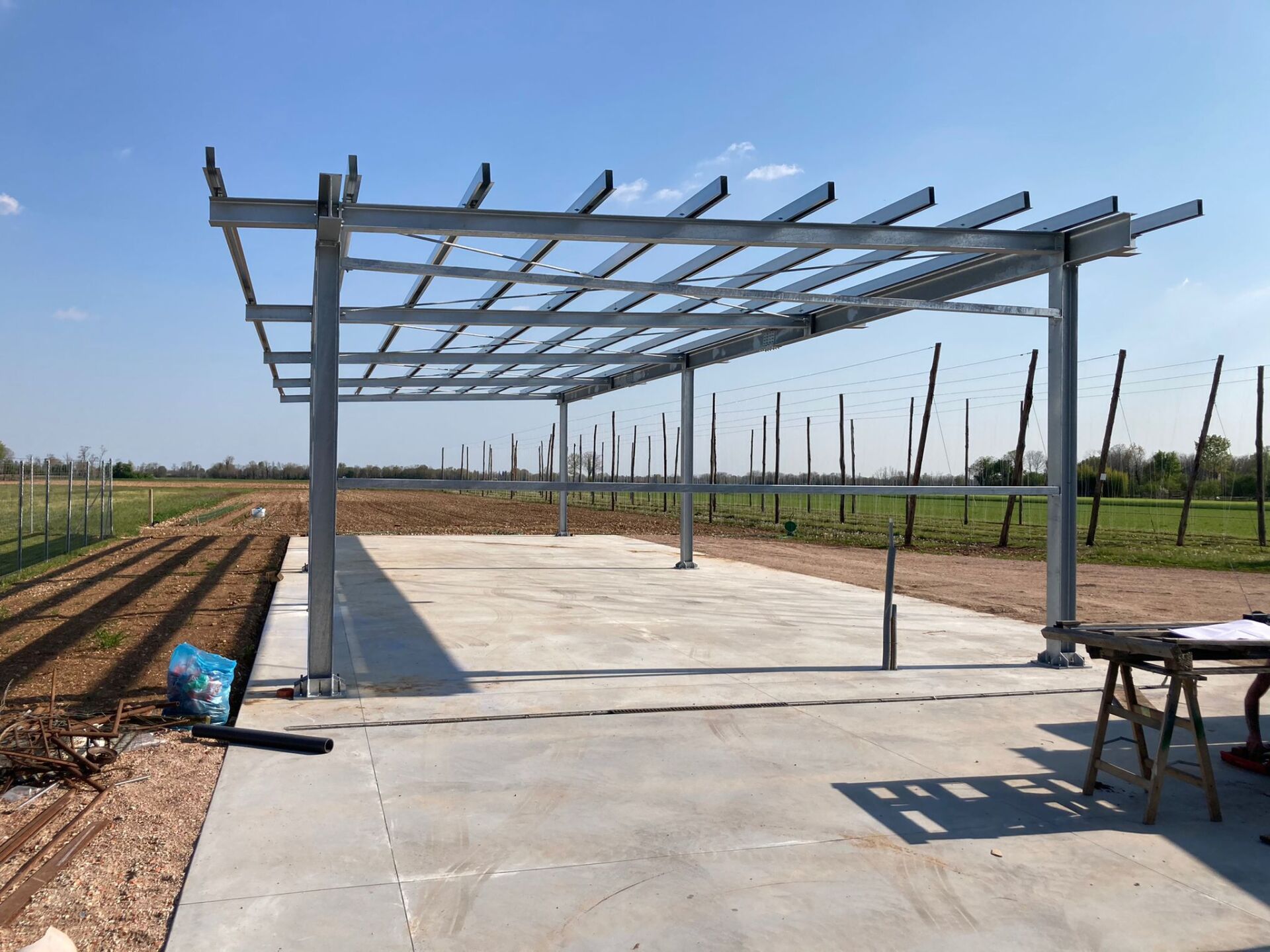 Pergola con struttura in acciaio su soletta di cemento in costruzione in un campo rurale.