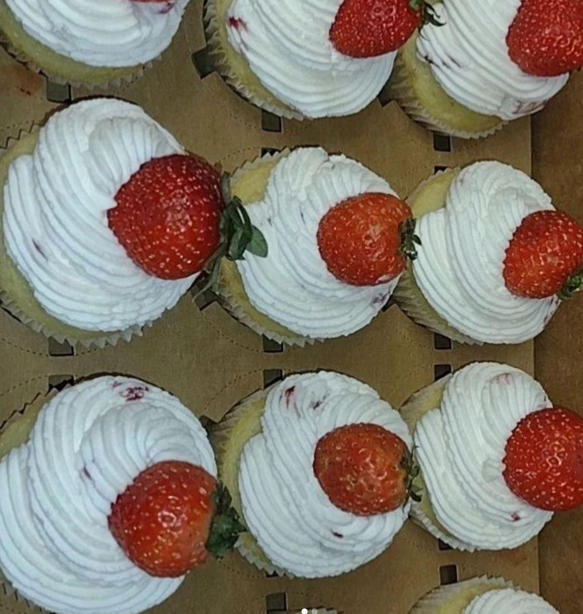 A box of cupcakes with whipped cream and strawberries on top
