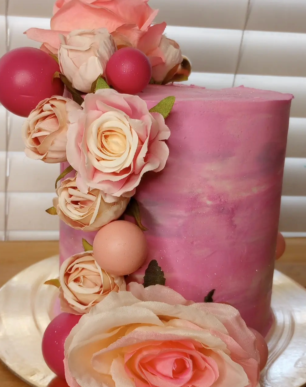 A pink cake decorated with pink roses and pink balls