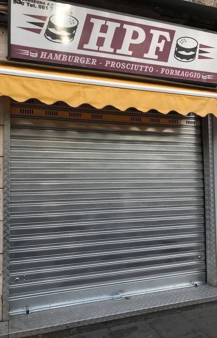 Serranda di un negozio di metalli chiusa sotto l'insegna HPF sulla vetrina.