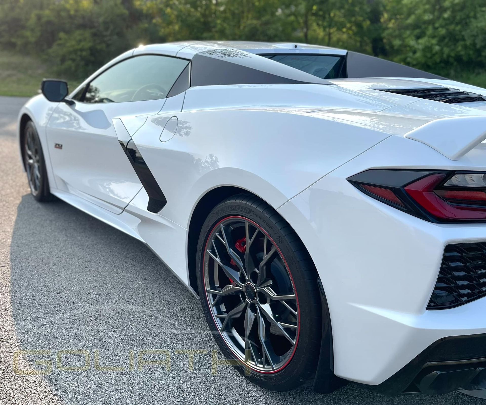 a white sports car with red wheels is parked on the side of the road .