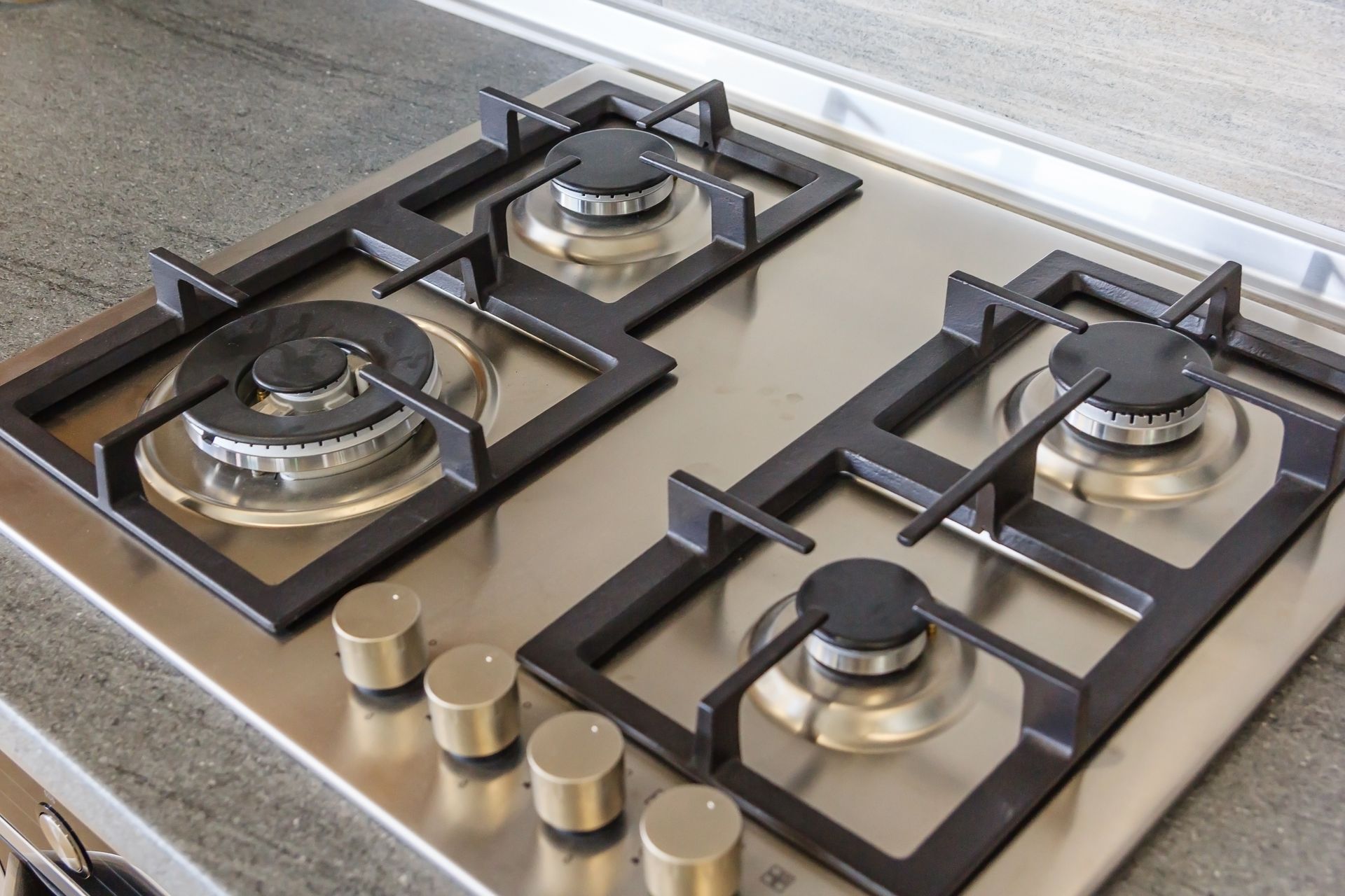 Modern four-burner gas cooktop with black grates and silver control knobs on a countertop