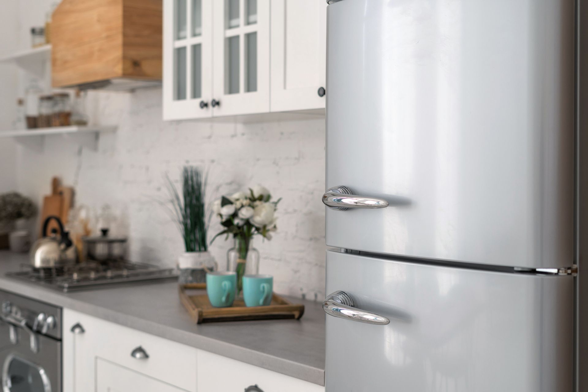 Modern kitchen with stainless steel fridge, white cabinets, gray backsplash, and decorative countertop accents