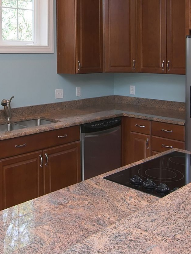 Small kitchen with brown cabinets, granite countertops, sink, dishwasher, and black cooktop.