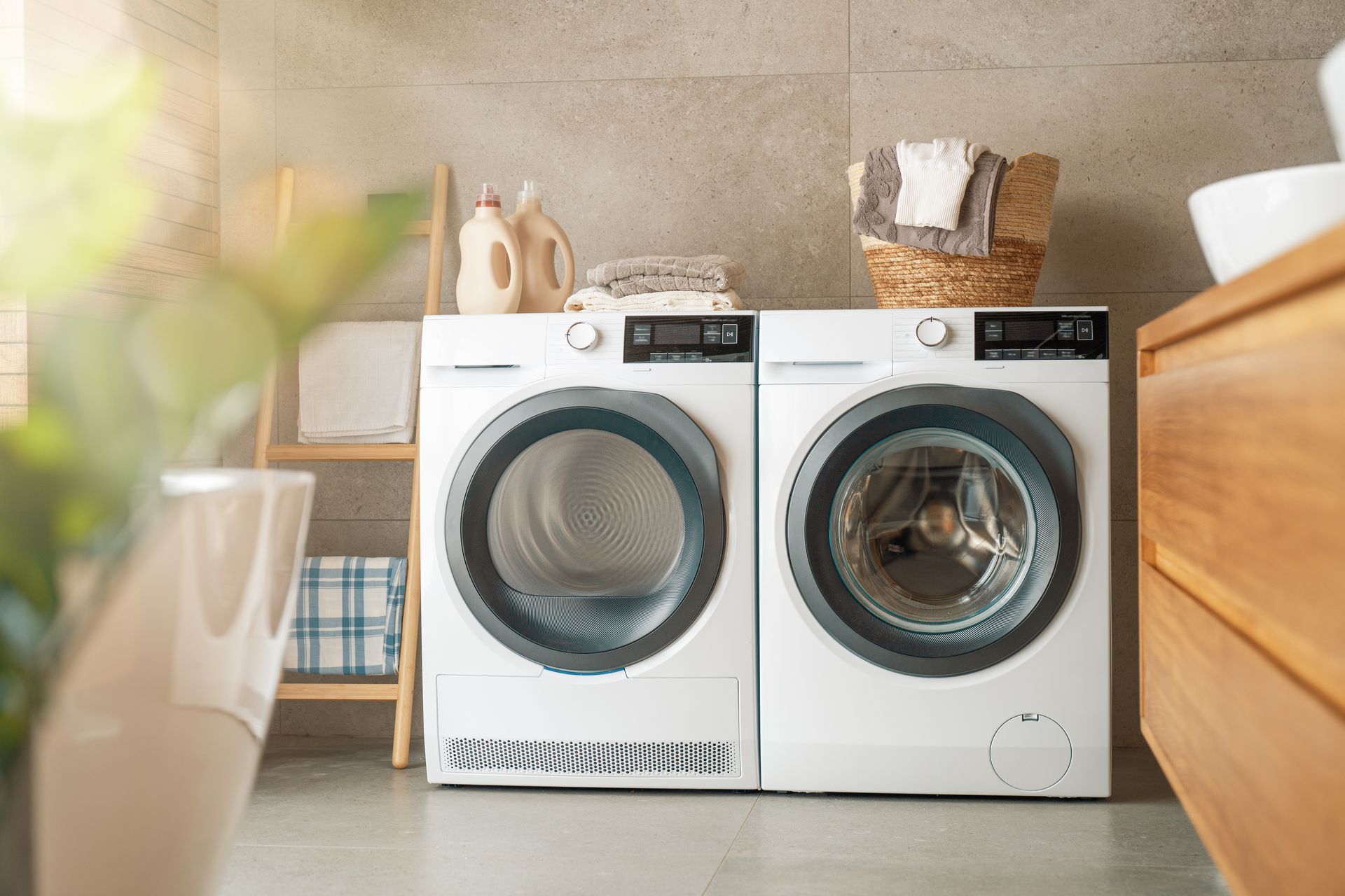 Two front-loading washing machines in a bright laundry room, with a basket and folded towels on top.