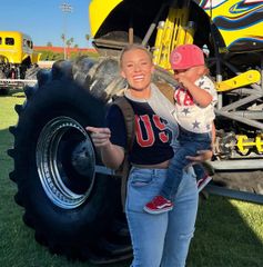 A woman is holding a baby in front of a monster truck