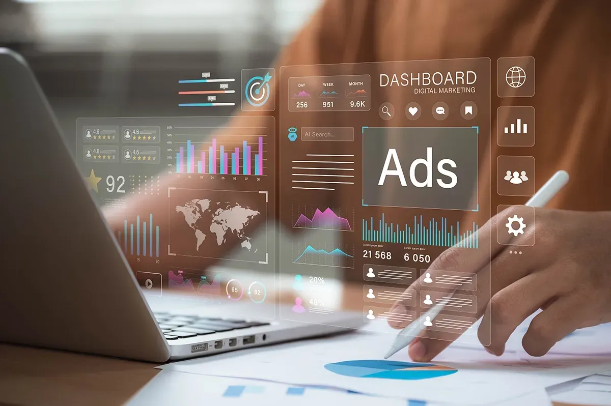 Hands using a laptop with floating digital ads and analytics charts over a desk