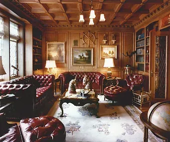 Elegant living room with red leather sofas, framed art, lamps, and wood-paneled walls