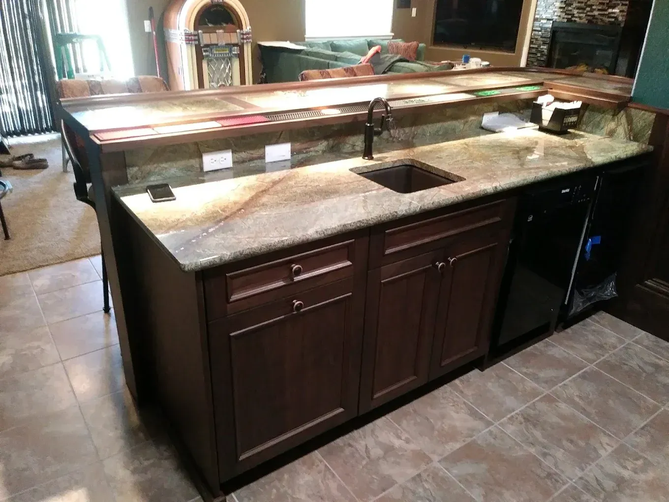 Kitchen island with dark wood cabinets, granite countertop, and built-in sink in a tiled kitchen