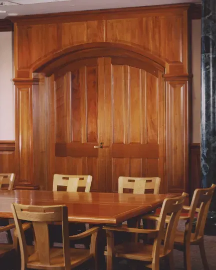 Wood-paneled dining room with a wooden table and chairs in front of double doors