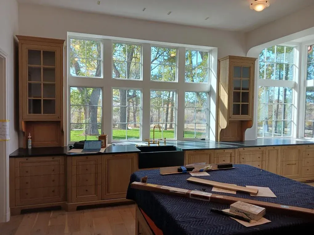 Bright kitchen with large windows, wood cabinets, and a blue-covered island with books and papers.