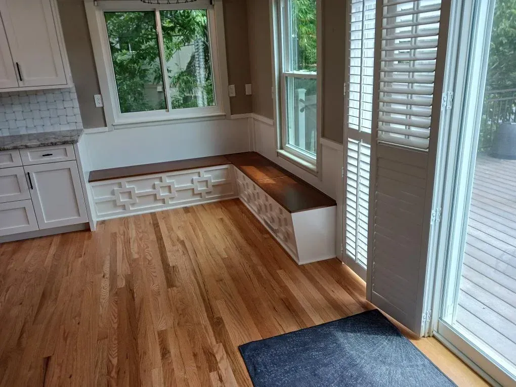 Bright empty kitchen with hardwood floors, white cabinets, a window seat, and sliding glass doors with shutters