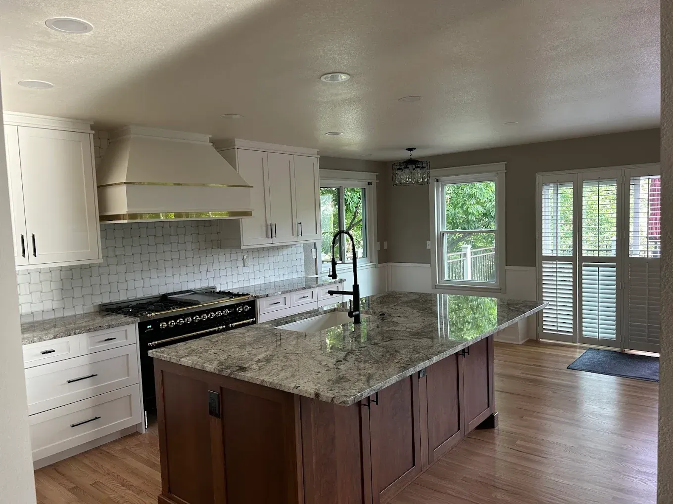 Bright kitchen with white cabinets, granite island, stainless stove, and French doors to a patio.