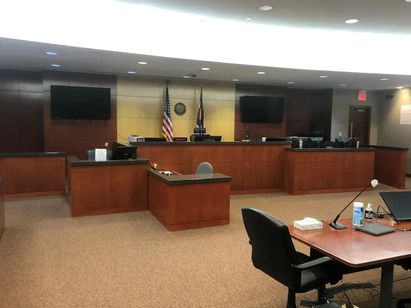 Empty courtroom with wooden benches, judge’s bench, and American flag at the front.