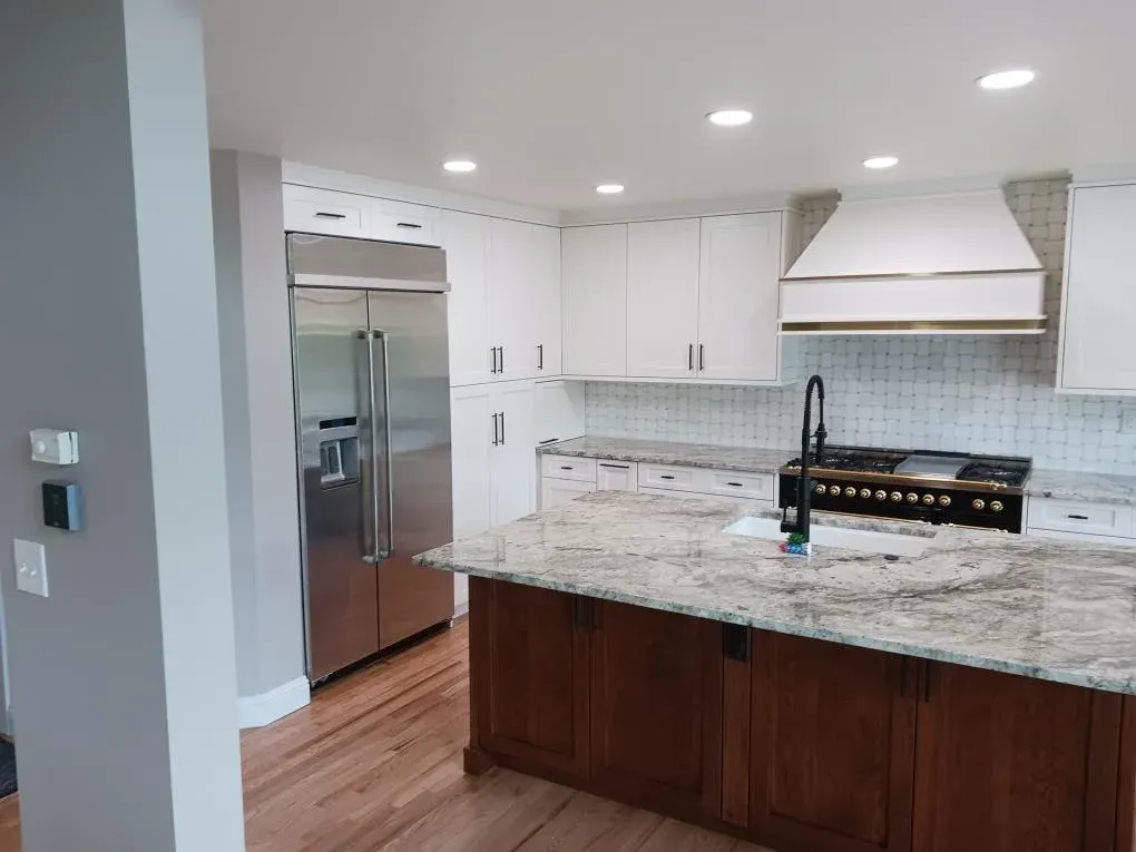 Modern white kitchen with stainless appliances, granite island, dark wood cabinets, and recessed lighting