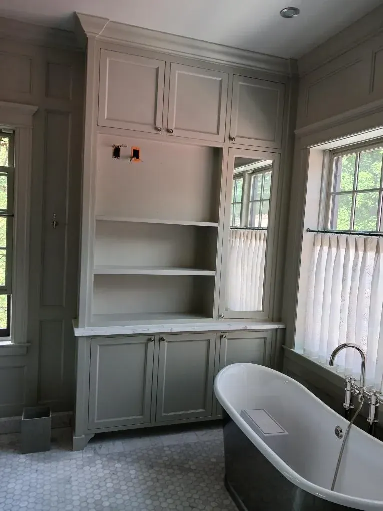 Bright bathroom with built-in white cabinetry and shelves beside a freestanding tub and window.