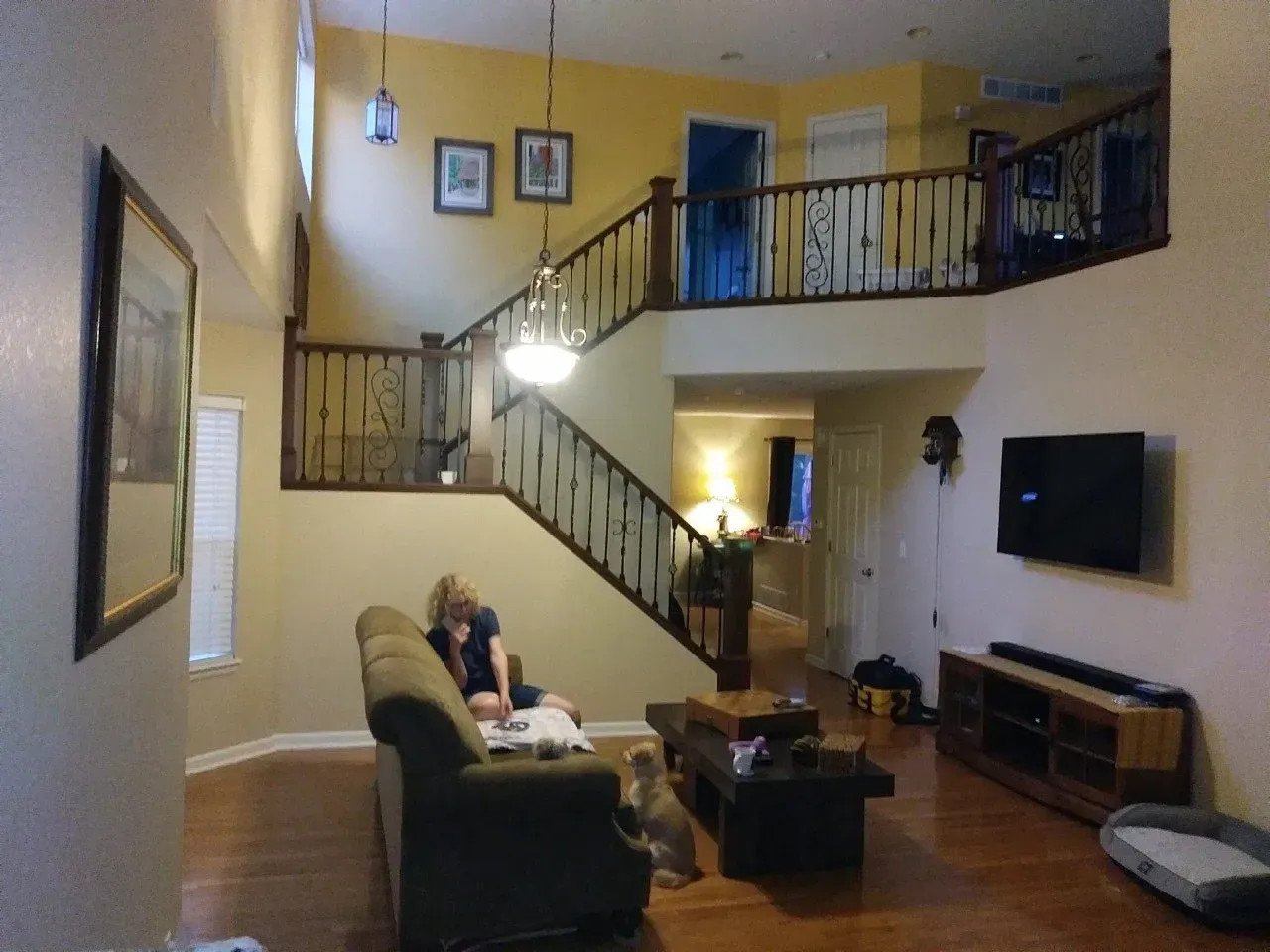 Living room with staircase, sofa, coffee table, wall TV, and an upper balcony railing