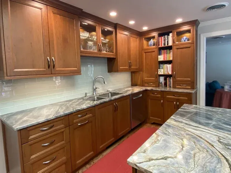 Modern kitchen with wood cabinets, marble countertops, under-cabinet lights, and red runner rug