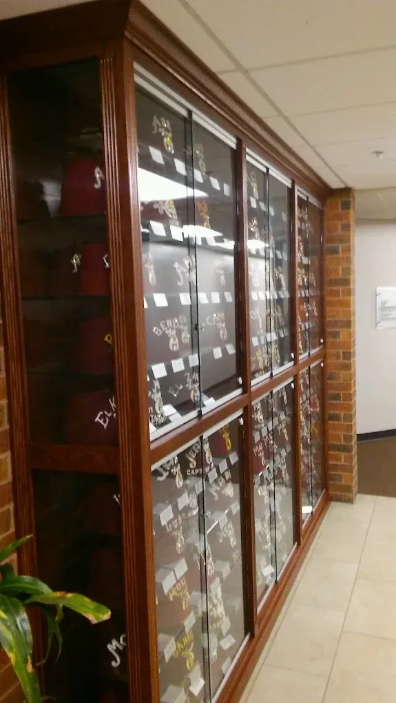 Wooden display cabinet with glass doors, filled with rows of small items in a tiled hallway.