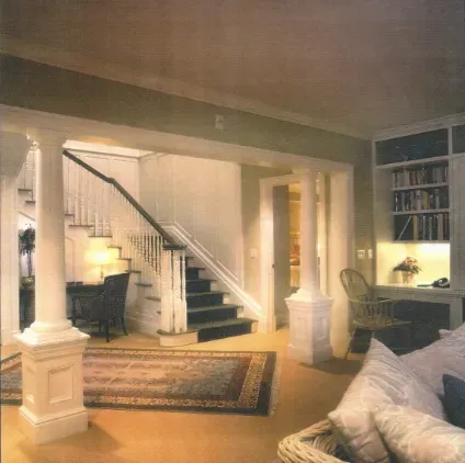 Elegant foyer with staircase, white columns, patterned rug, desk nook, and sofa in warm lighting