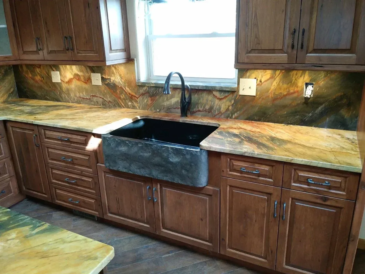 Kitchen with wooden cabinets, black sink, tan stone countertops, and a window above the sink.