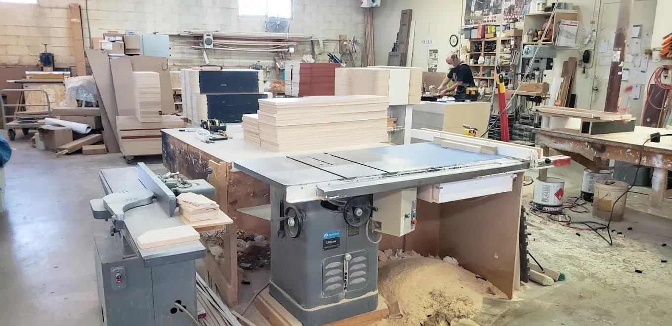 Woodworking shop with a large table saw, lumber stacks, and sawdust on the floor