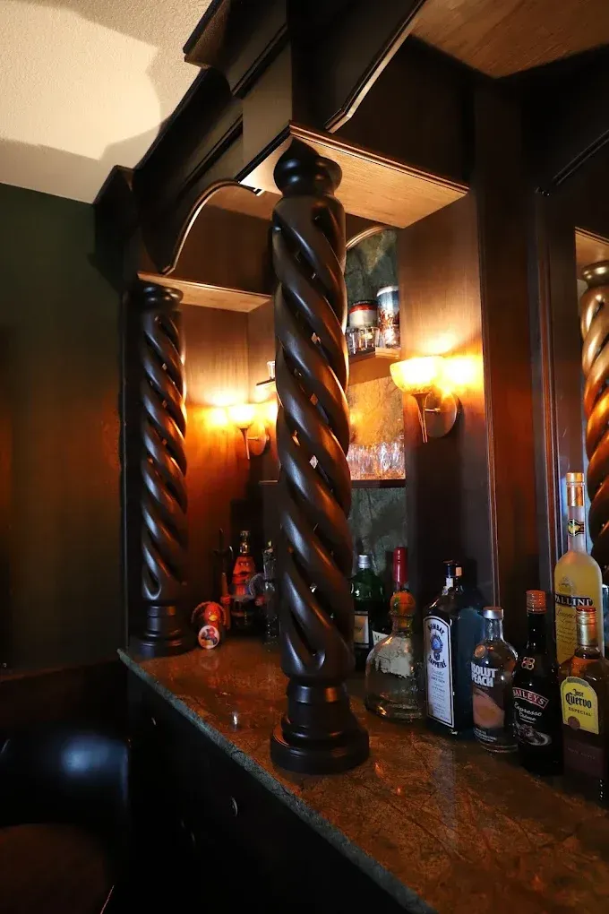 Dimly lit bar with twisted wooden columns, bottles on the counter, and a warm amber glow