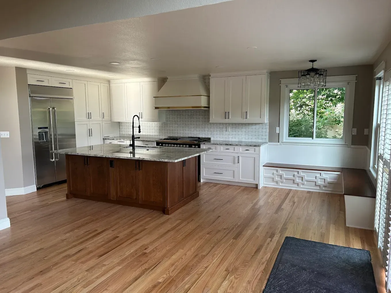 Bright kitchen with white cabinets, wood island, stainless fridge, and large window seat on hardwood floors