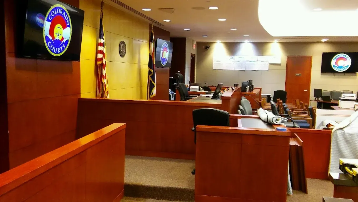 Courtroom interior with wooden benches, judge’s bench, flags, and law enforcement emblems.
