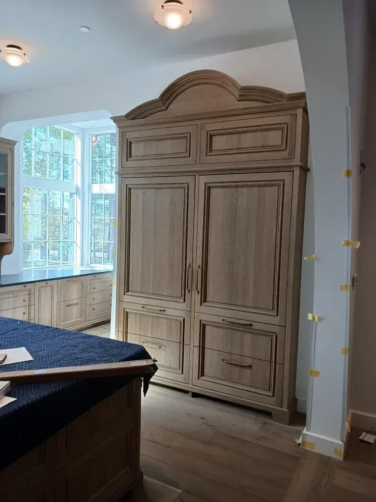 Large rustic wooden armoire in a bright room near a window and dark countertop.